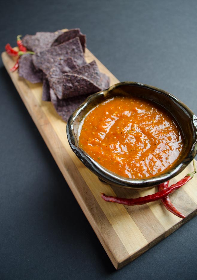 chile de arbol salsa on a wooden board with blue corn chips