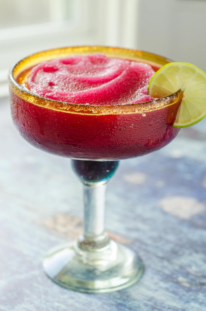 Frozen pink margarita in glass with lime and salt.