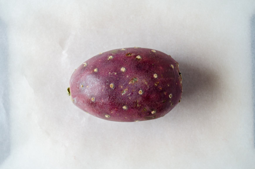 A whole red prickly pear on a white background.