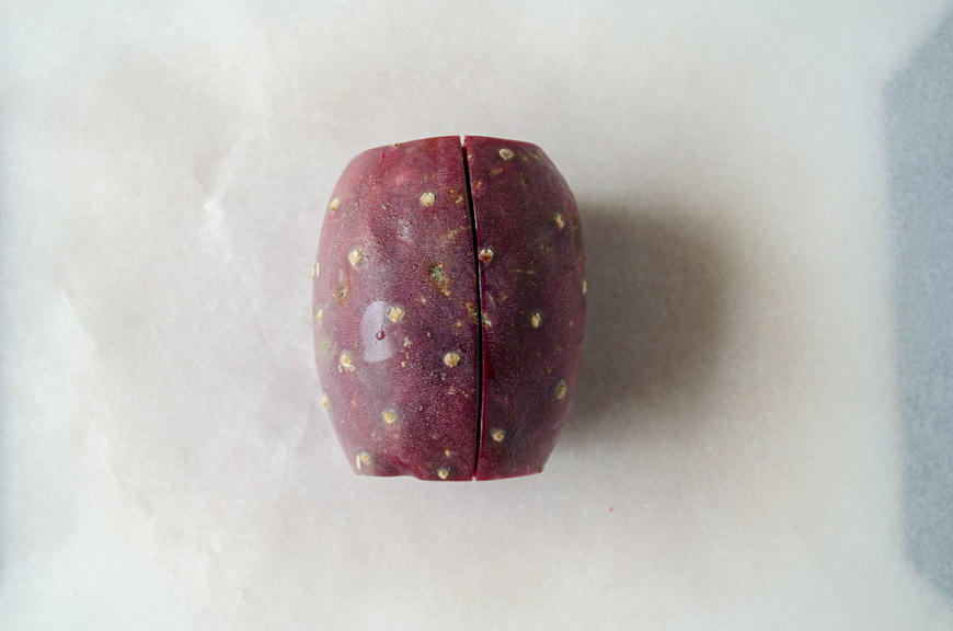 A red prickly pear on the counter sliced in half long ways.