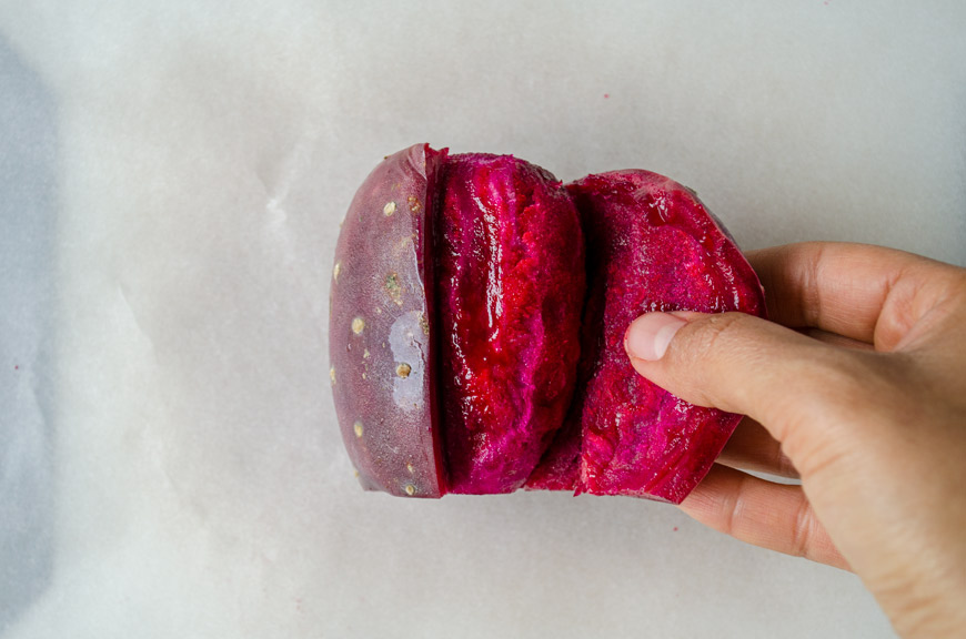 A hand peeling back the skin of a red prickly pear.