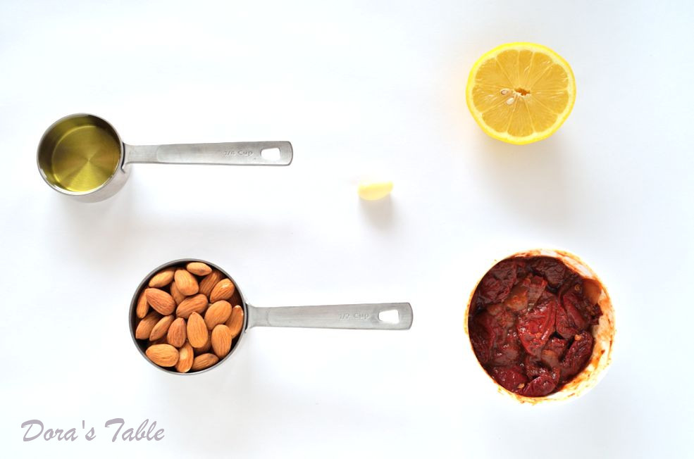 Measuring cups of almonds, chile peppers and olive oil on a white surface.