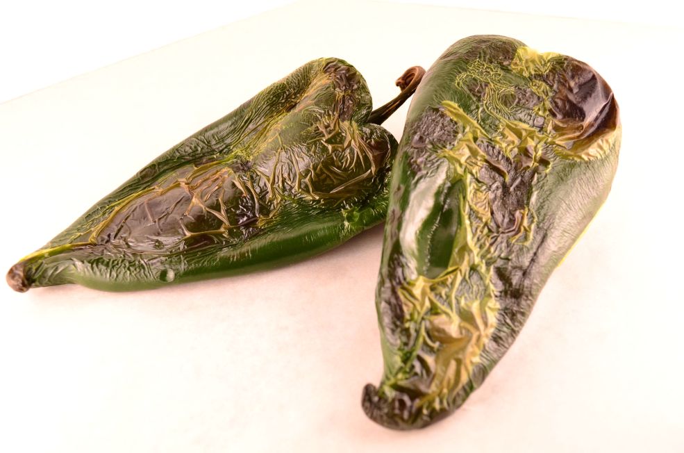 Two roasted poblano peppers on a white surface.