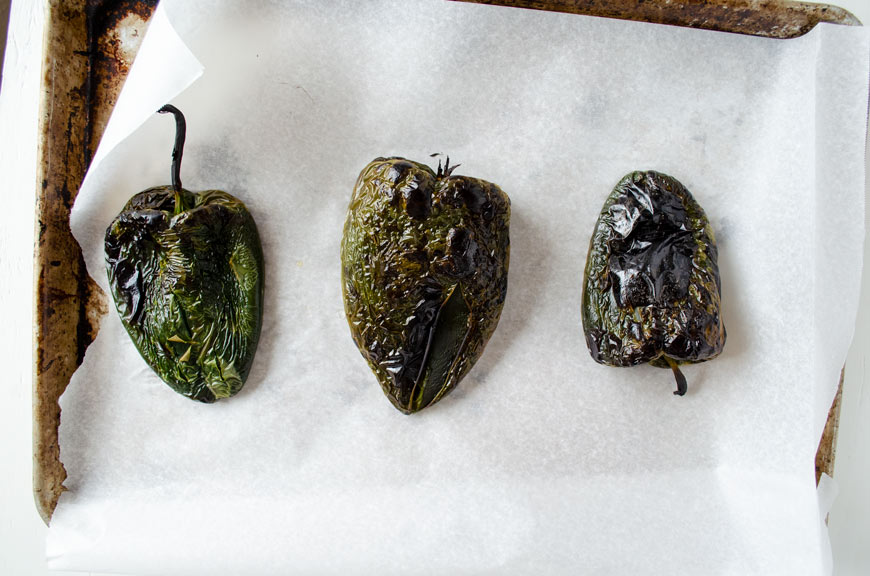 Roasted poblano peppers on a sheet tray with parchment paper.