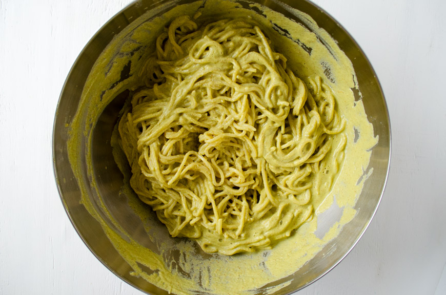 Espagueti verde being tossed in a stainless steel bowl.