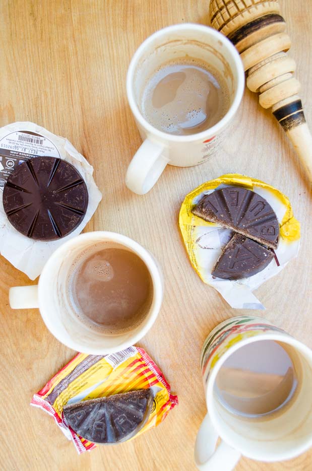 Top view of Mexican chocolate wedges on their wrappers next to mugs of warmed milk and chocolate.