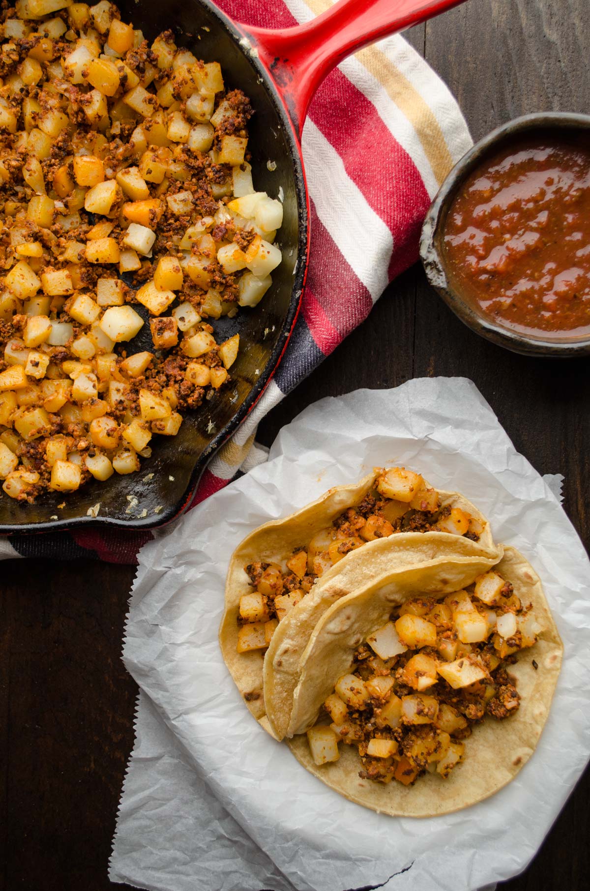 Vegan potato and chorizo tacos on a plate next to a skillet of filling.