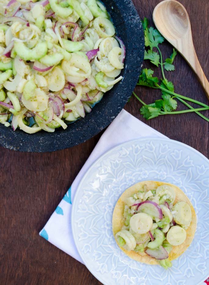 Aguachile in a molcajete next to a plate with a taco topped with hearts of palm ceviche.