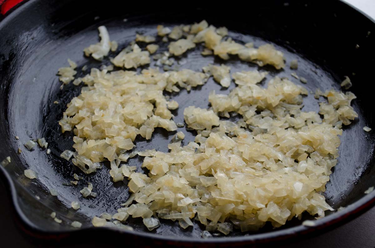 Diced onions sweating in a cast iron skillet.