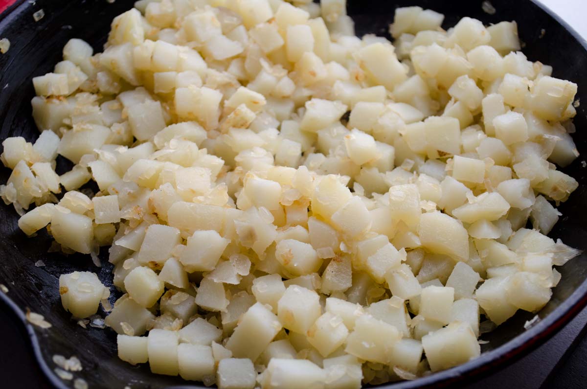 Diced potatoes cooking in a cast iron skillet.