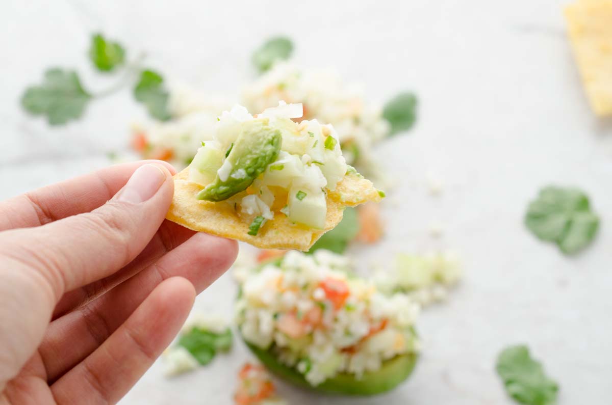 A hand holding a tortilla chip topped with cauliflower ceviche.