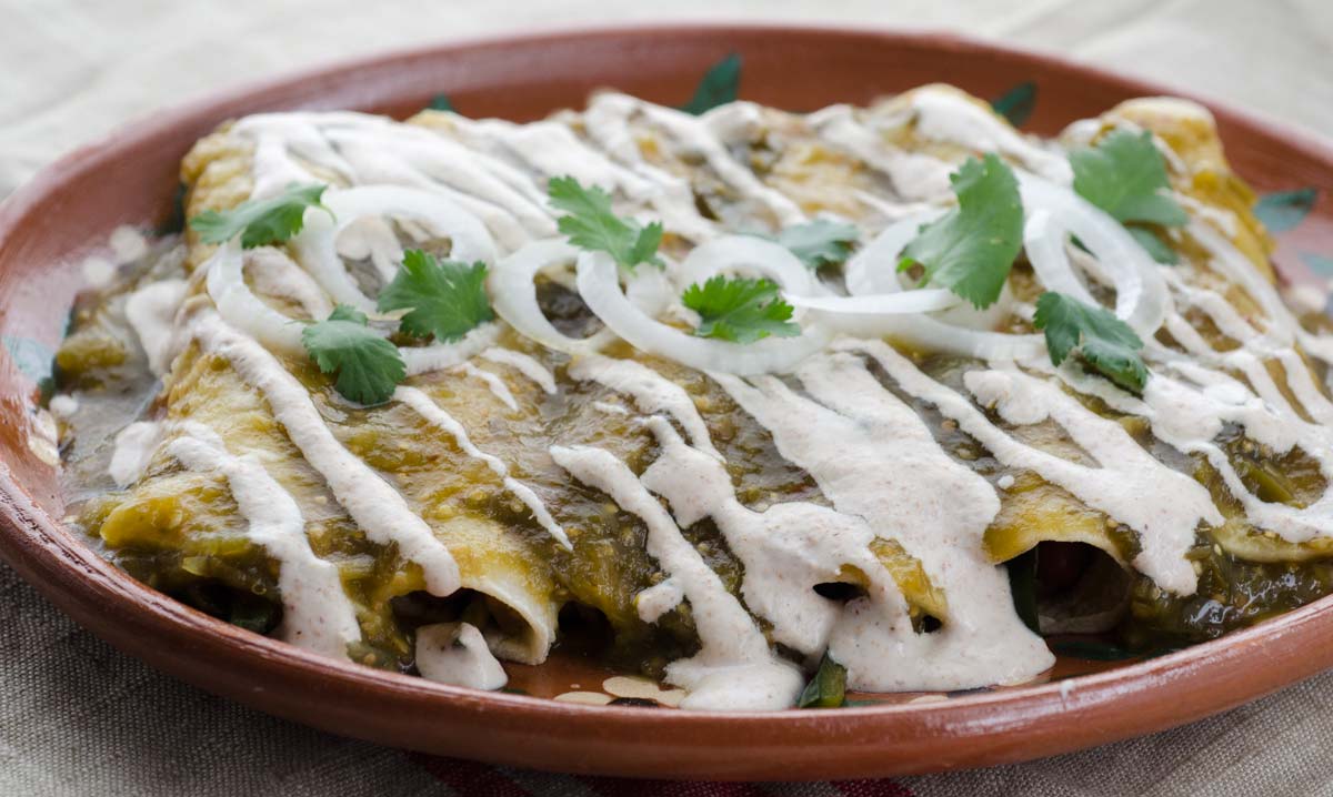 Vegan roasted tomatillo enchiladas, filled with sautéed onions, garlic, poblano peppers, and pinto beans. Bathed in salsa and almond crema.