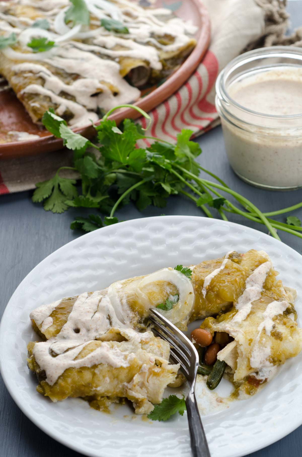 Vegan roasted tomatillo enchiladas, filled with sautéed onions, garlic, poblano peppers, and pinto beans. Bathed in salsa and almond crema.