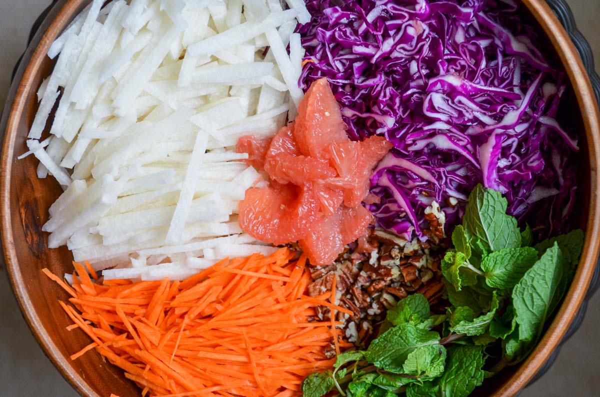 Julienned vegetables in a brown salad serving bowl topped with grapefruit and pecans.