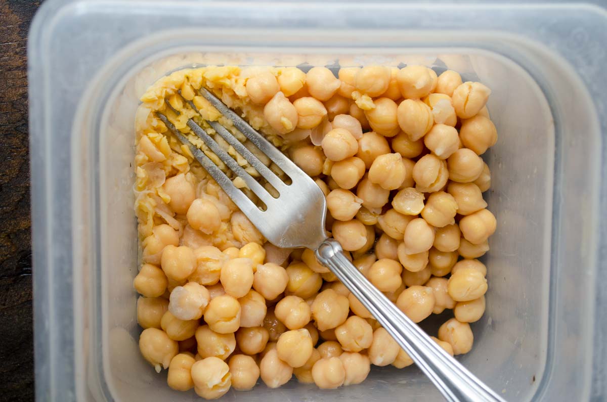 A fork mashing cooked chickpeas.