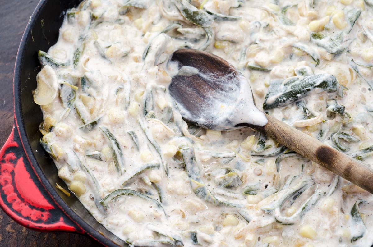 Vegan Rajas con Crema Taco filling with a wooden spoon in a cast iron skillet.