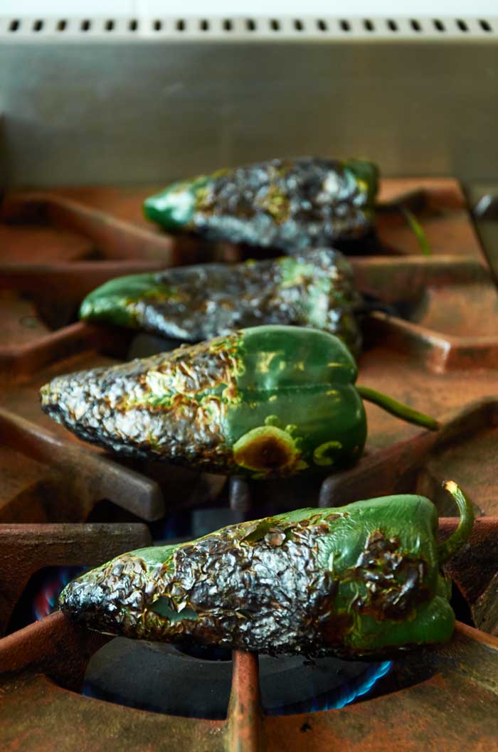 Poblano peppers charring on a gas stovetop.