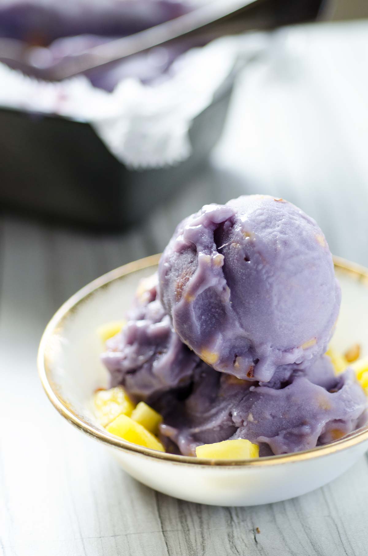 Purple sweet potato ice cream over chopped pineapple in a small bowl.