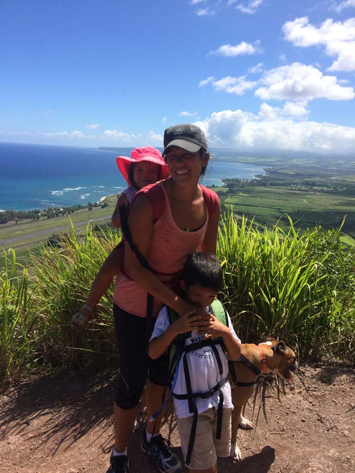 Mom and two kids on a grassy hill with the ocean in the background.