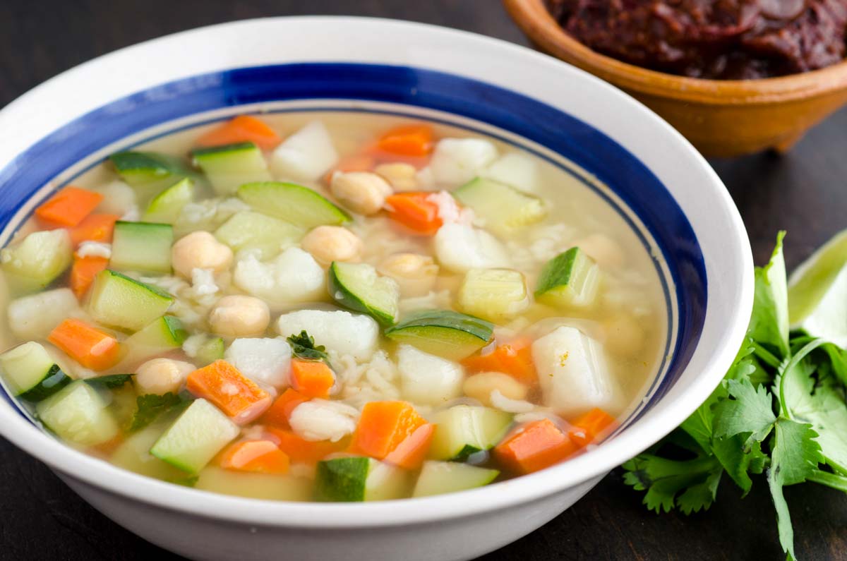 Close up of white bowl with blue rim filled with soup zucchini, carrots, chickpeas and rice.