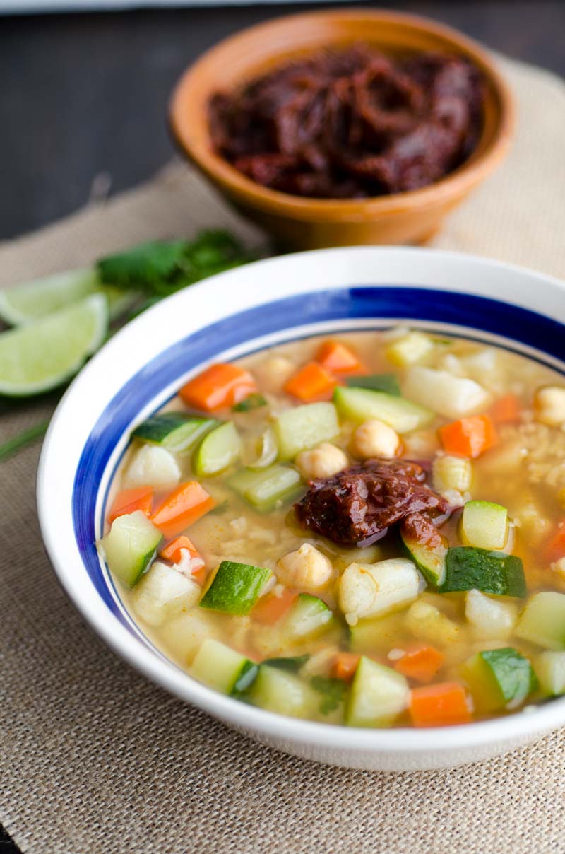 White bowl with blue rim filled with authentic caldo tlalpeño soup zucchini, carrots, chickpeas and rice.