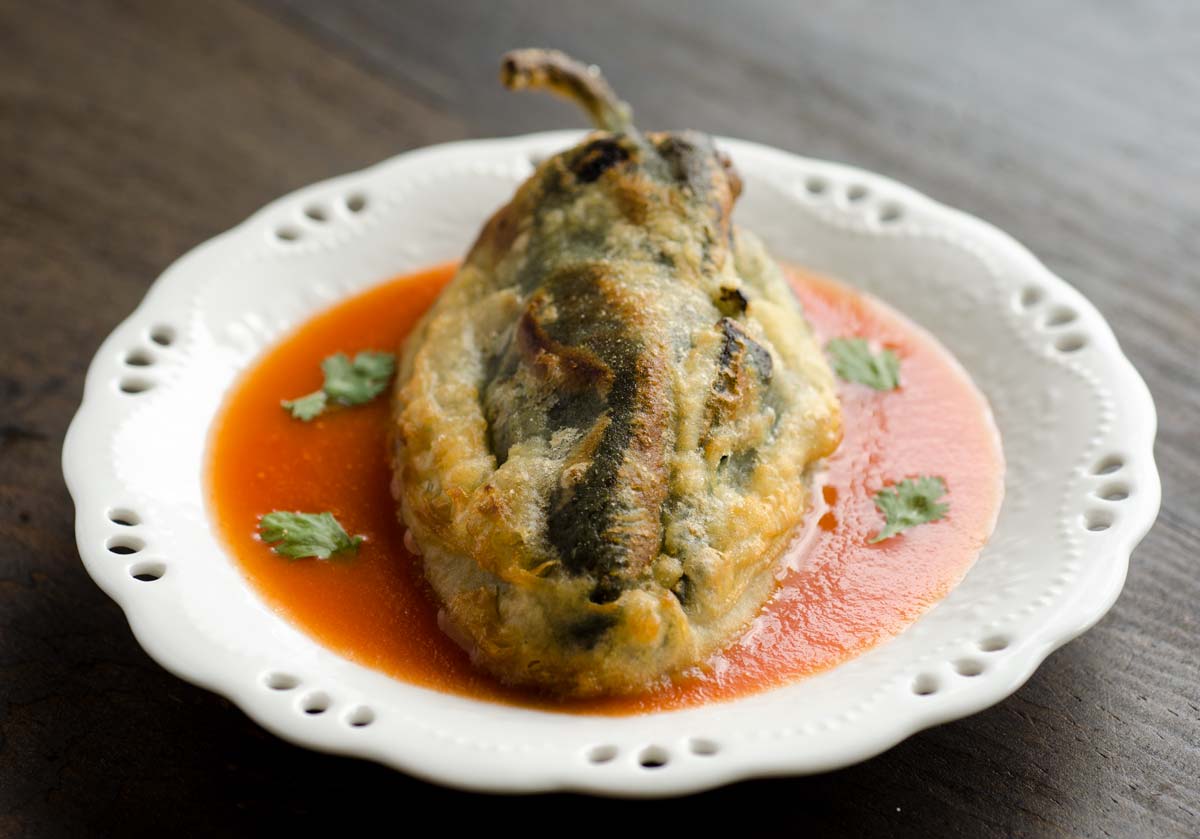 A vegan chile relleno with red sauce in a shallow white bowl.