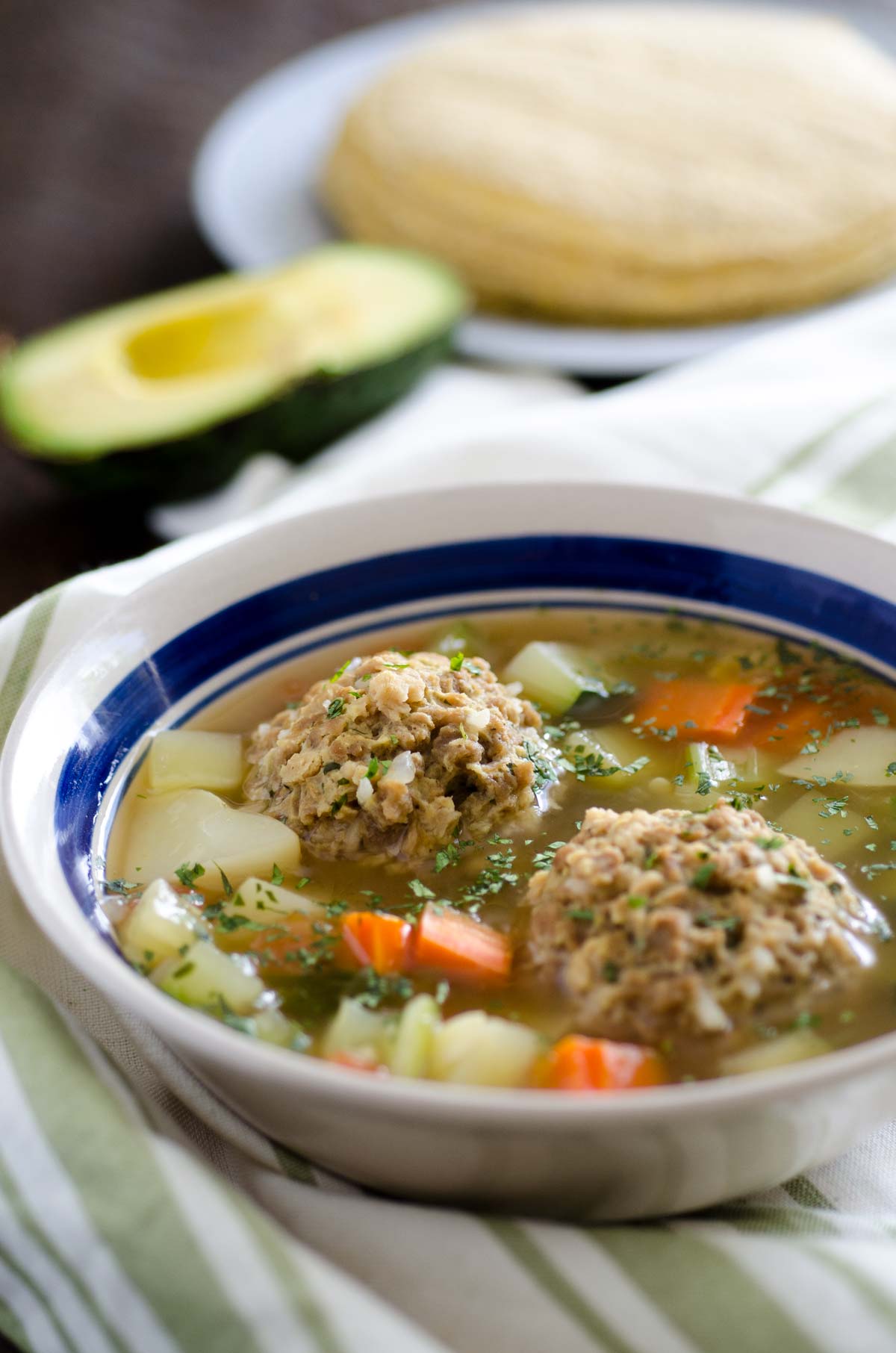 Vegan Mexican meatball soup in a small blue and white striped bowl.