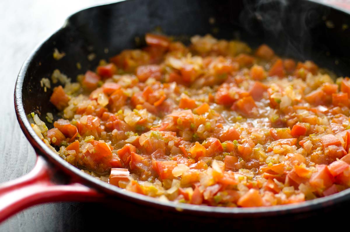 Finely diced tomatoes, onions, and peppers in a cast iron skillet.