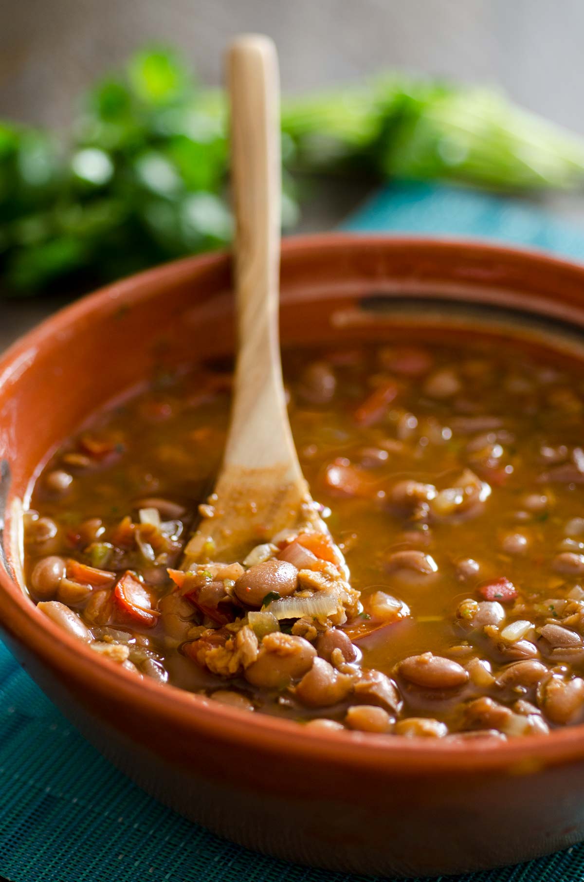 Wooden spoon in a brown clay bowl of Vegan Frijoles Charros.