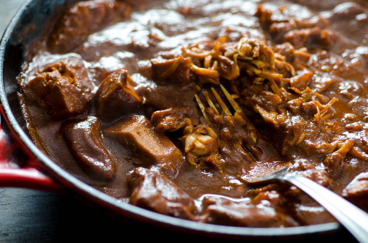 Jackfruit simmering in red chile sauce in a cast iron pan