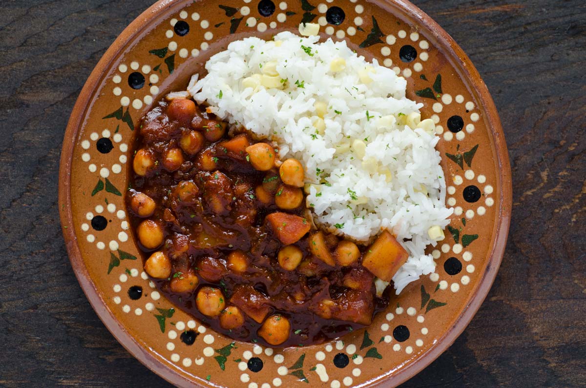 Over head shot of sweet potato and chickpea stew with white rice on a Mexican clay plate.