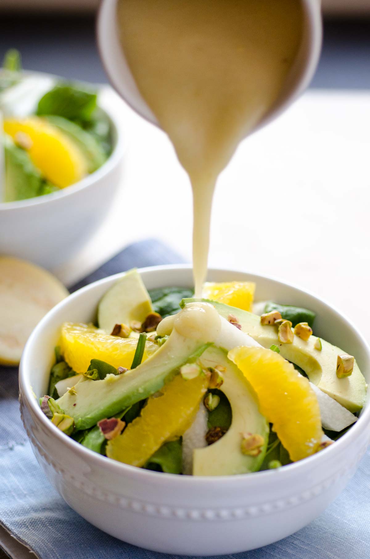 Dressing being poured over a small white bowl of Spinach Avocado Jicama Salad.