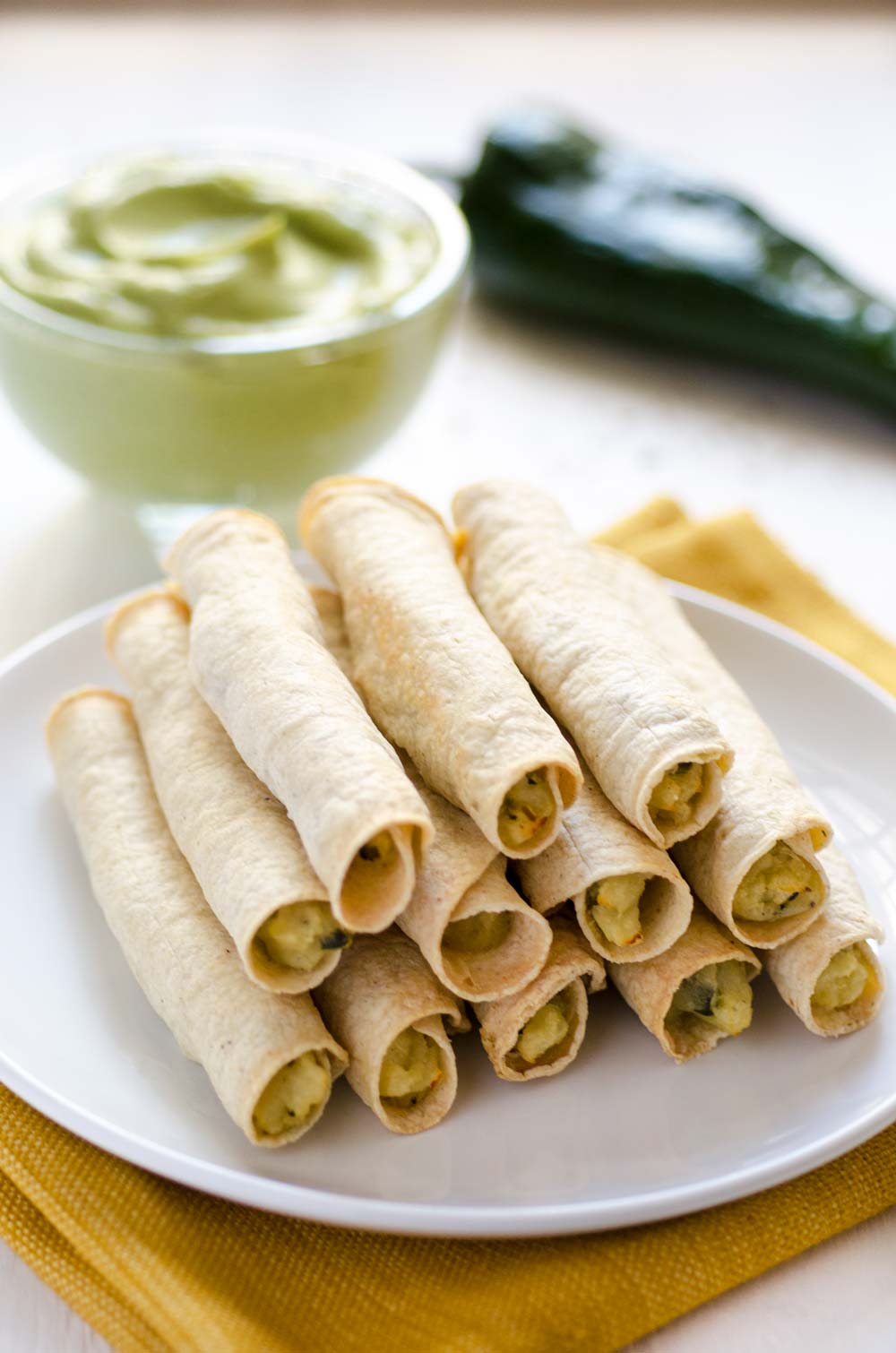 Stack of potato poblano flautas on a white dinner plate.