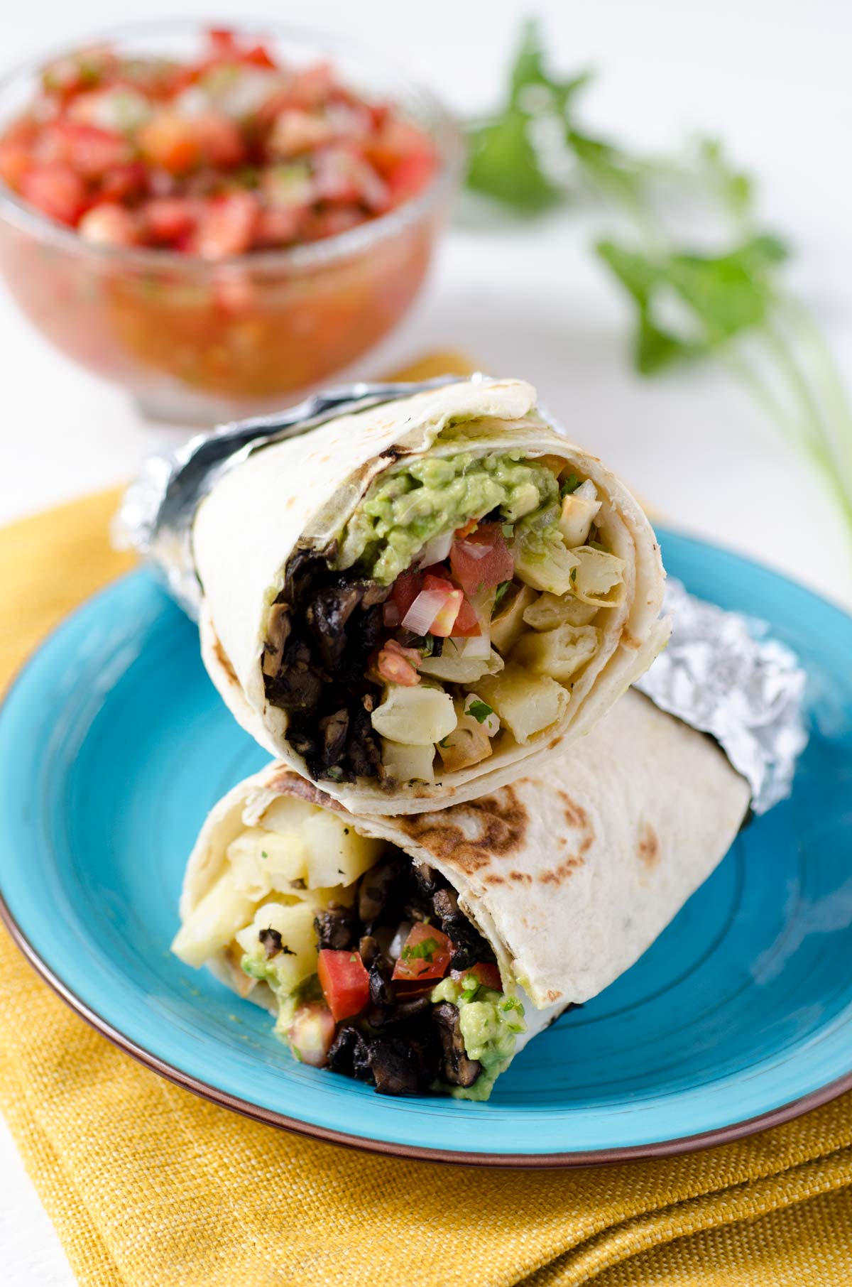 Close up view of a California black bean burrito cut in half on a blue plate.