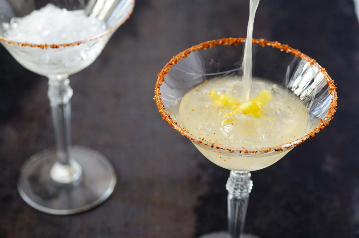 Pineapple chile margarita being poured on the rocks in a martini glass.