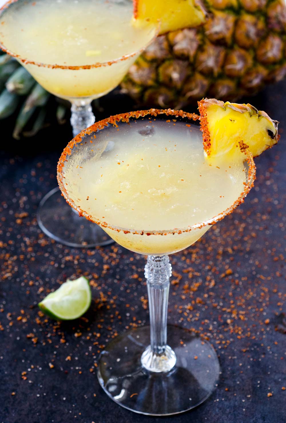 A pineapple chile margarita on the rocks in a martini glass with a pineapple wedge.