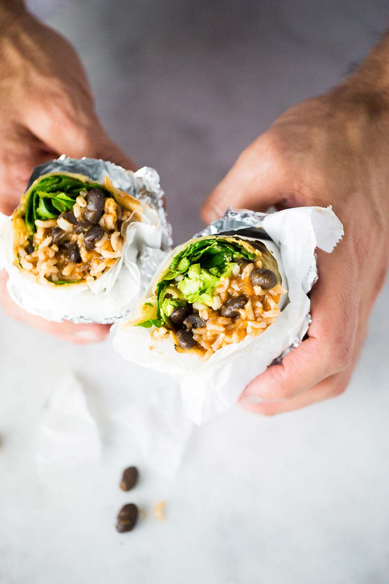 A pair of hands holding a split in half vegan bean and rice burrito.