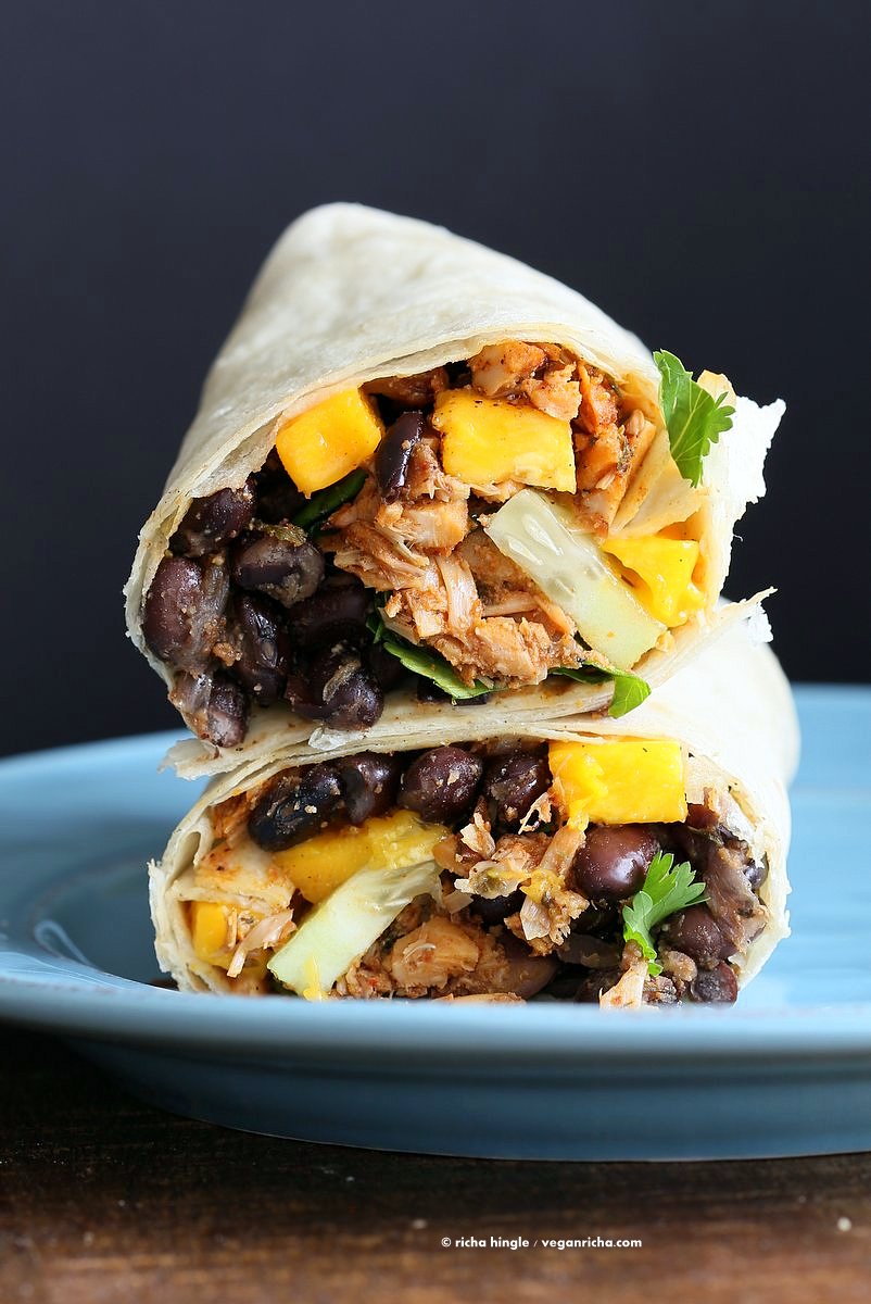 Close up view of a cut open burrito filled with mango, black beans, and jackfruit,