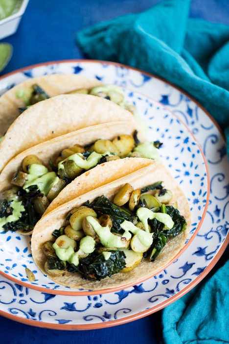 Kale potato tacos in corn tortillas on a blue and white patterned plate.