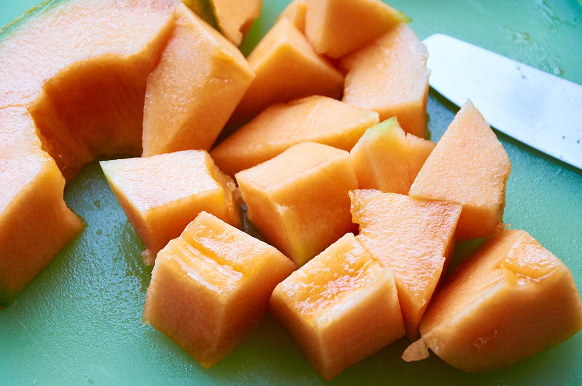 Diced cantaloupe on a green cutting board.