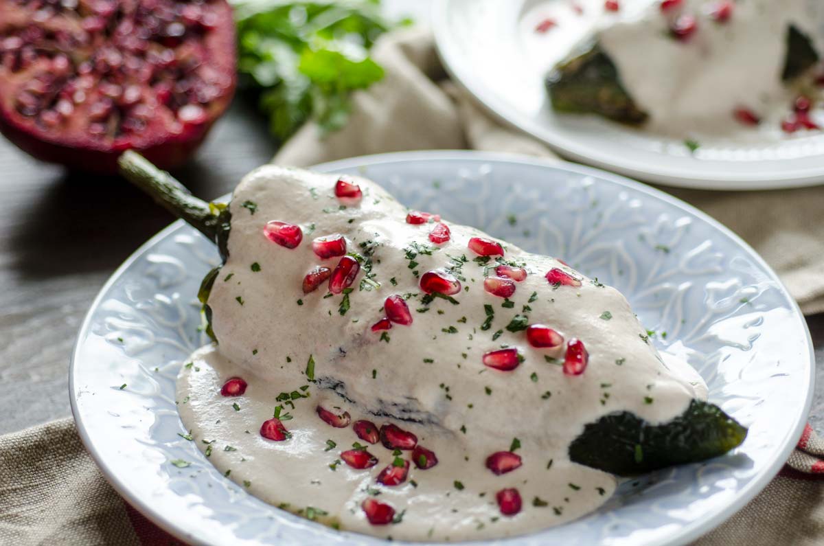 Vegan Chiles en Nogada, roasted poblano chile is stuffed with an aromatic picadillo, covered in walnut cream sauce and pomegranate seeds.