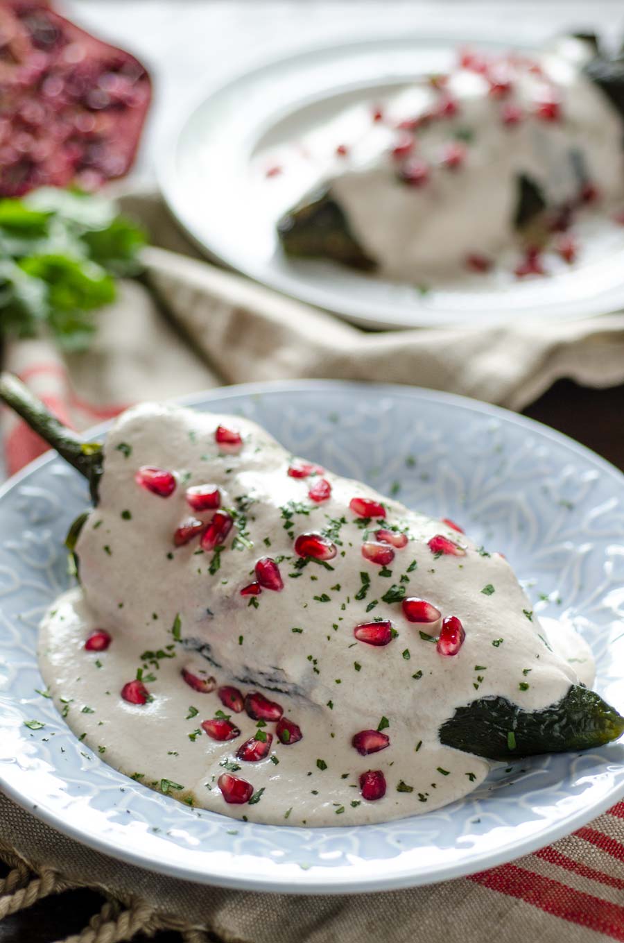 Roasted poblano topped with white sauce and pomegranate arils on a white plate.