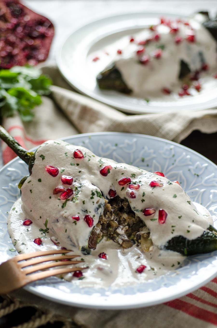 Roasted poblano topped with white sauce and pomegranate arils on a white plate.