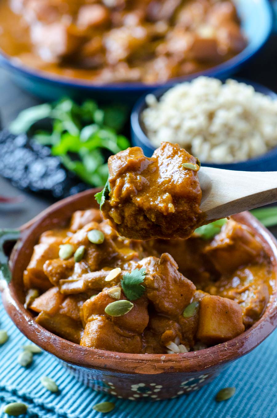 A wooden spoon lifting up a bite of Pipian Rojo Over Rice from a small brown bowl.