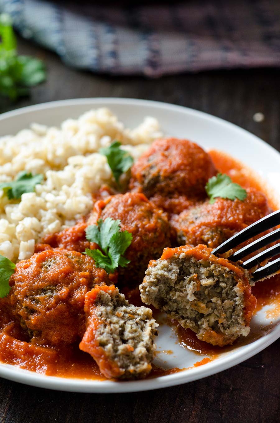 A fork showing off the inside of a tofu meatball covered with red sauce.