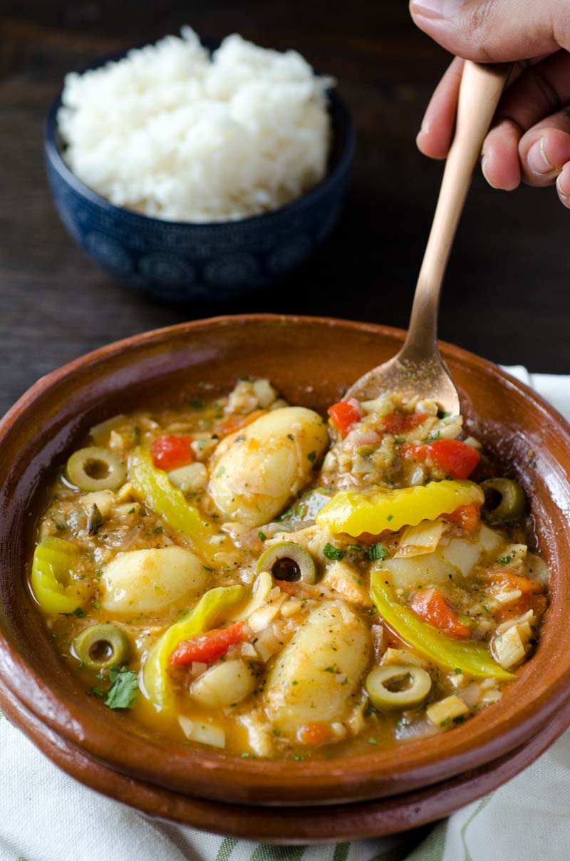 A spoon lifting up a bite of Vegan Bacalao a la Vizcaína from a brown bowl.