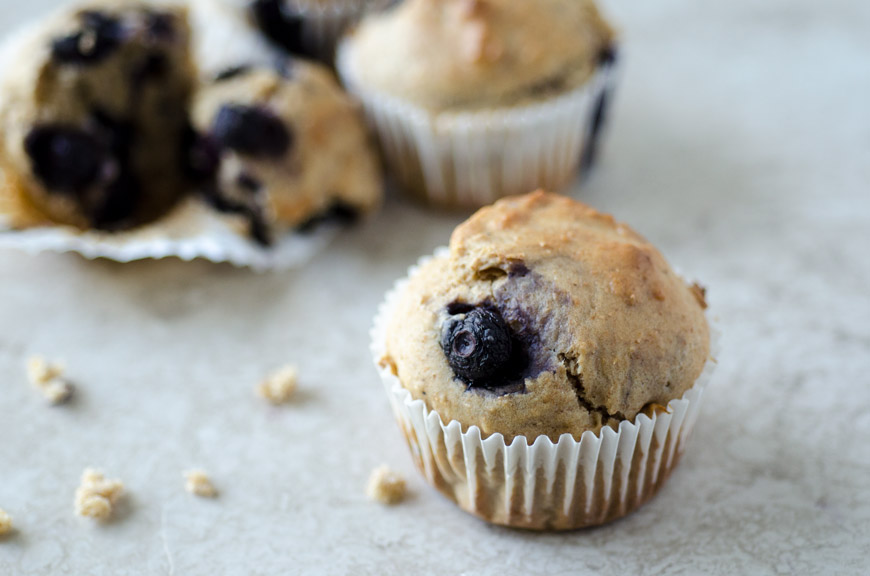 closeup of a vegan blueberry muffin with a giant blueberry peeking out of the top.