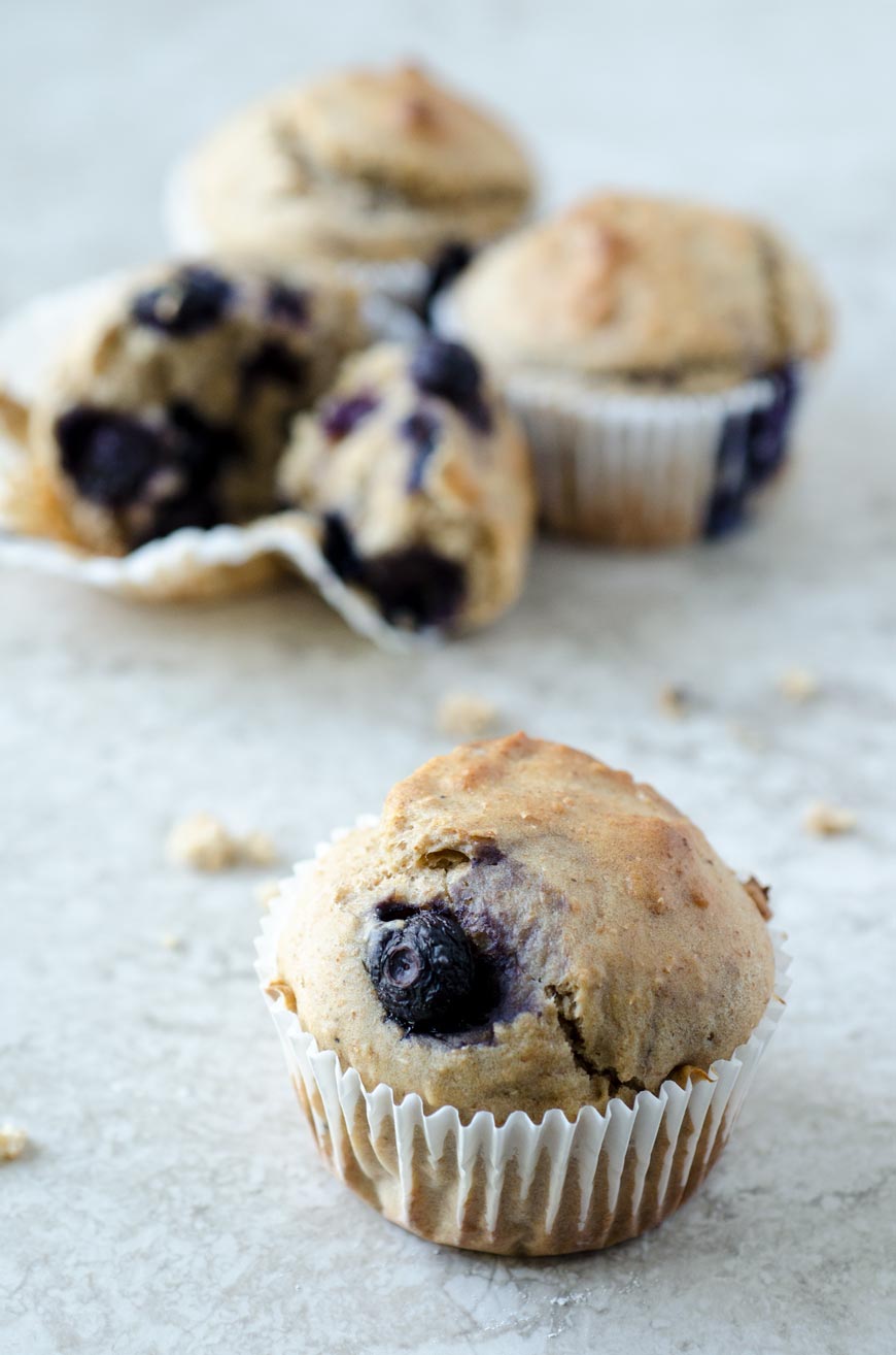 A blueberry muffin in focus with three blurred muffins in the background.