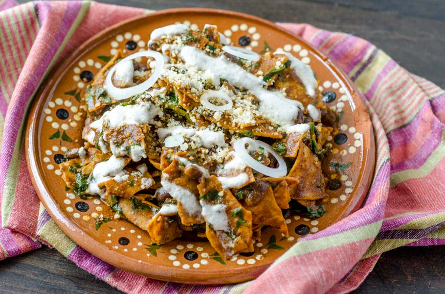 Vegan mole chilaquiles are tortilla chips covered in mole sauce and mixed with sautéed greens and black beans, then drizzled with an almond crema, and vegan queso cotija. The combination is seriously good.