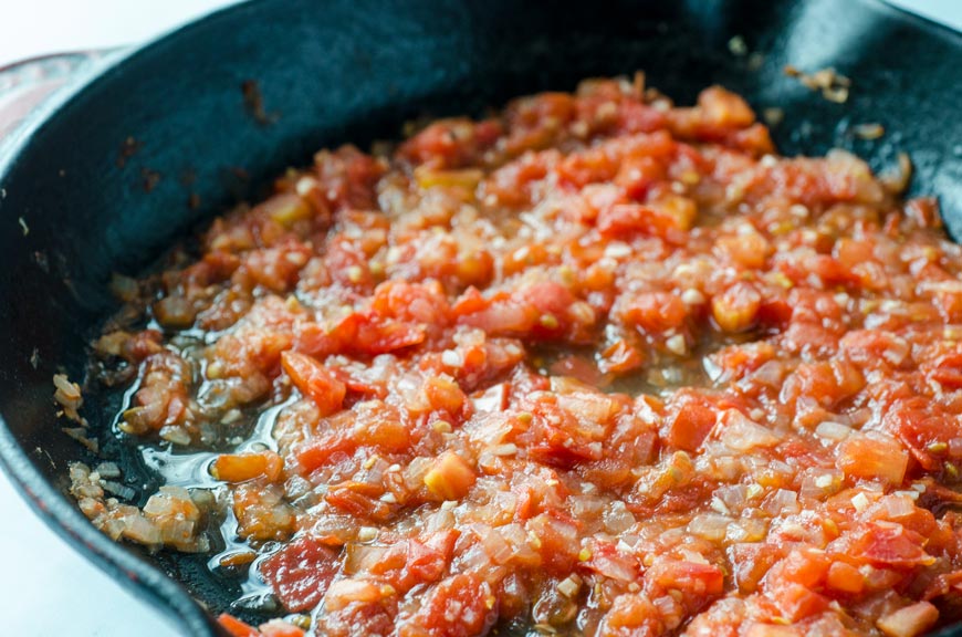 Tomatoes cooking down in a cast iron skillet.